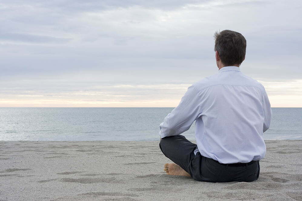 Businessman meditating on a beach at the sea